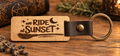 We Ride At Sunset Keychain in light engraved wood with a dark leather loop, brass ring, crescent moon, stars and broomstick