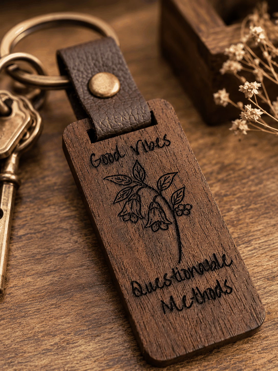Good Vibes keychain in dark rustic wood with engraved botanical illustration and lettering, leather loop and brass hardware