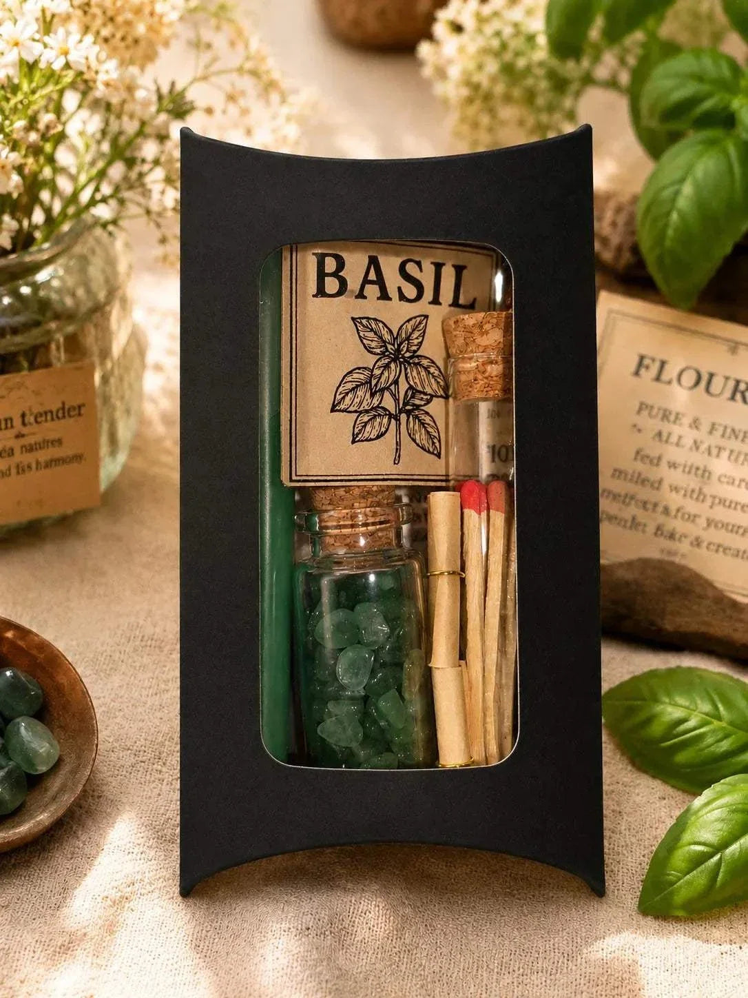 The Flourishing Spell Kit in a black windowed box, featuring a basil label, green crystals, wooden matches and corked vial