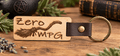Zero MPG Keychain in pale engraved wood with a flying broom design, dark brown leather loop and brass ring